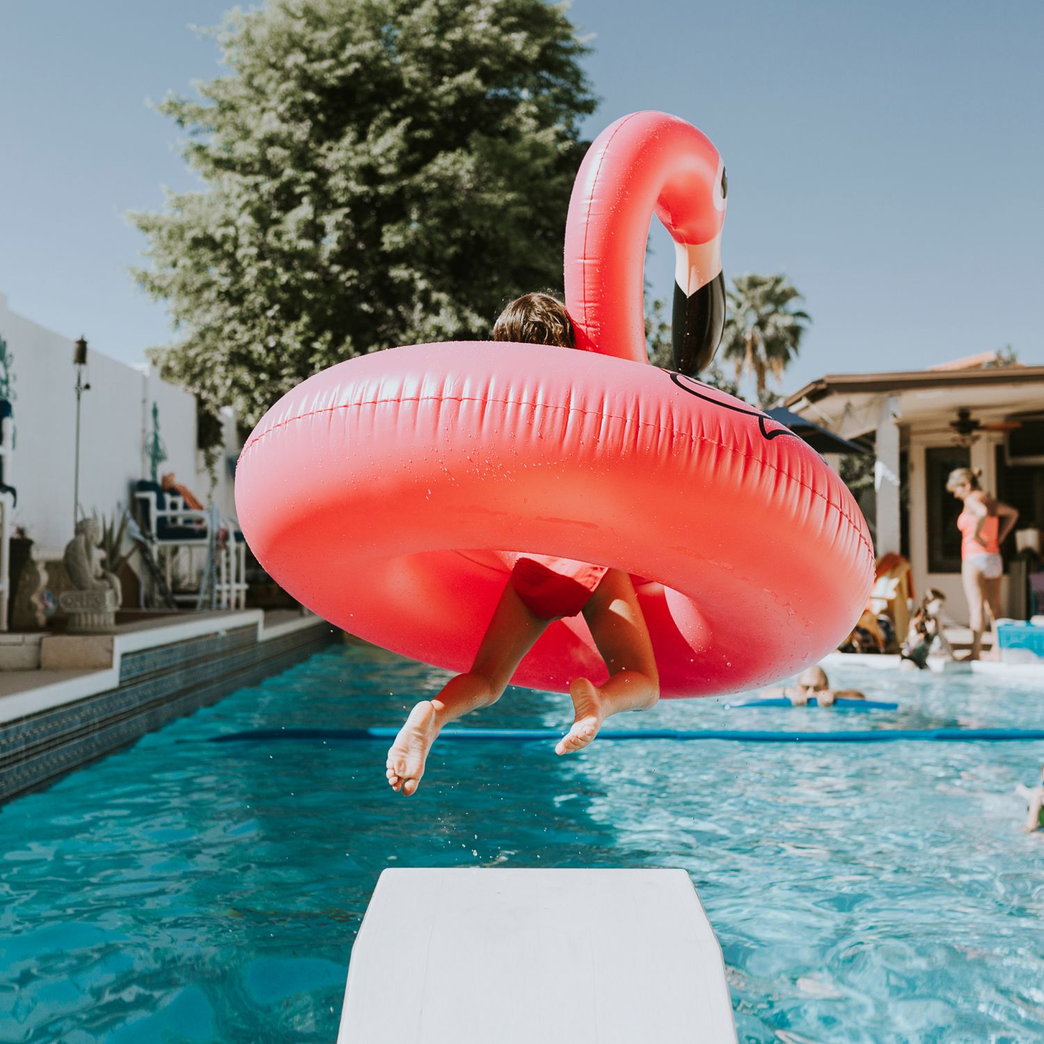 Rear view of girl jumping with a plastic flamingo into pool