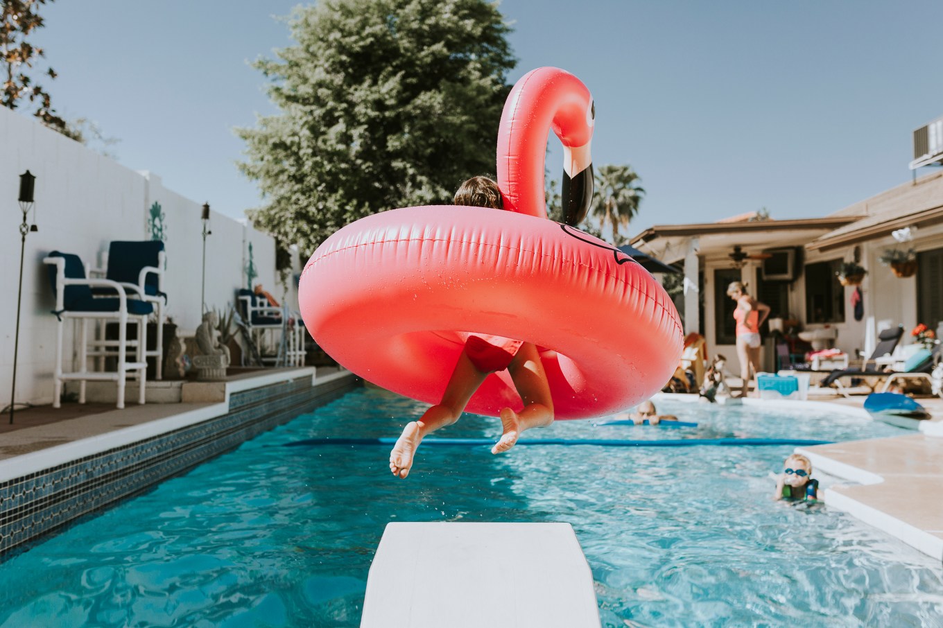 Rear view of girl jumping with a plastic flamingo into pool