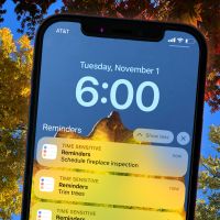 Variety of tress with colorful changing leaves of bright yellow orange red and gold in the background with a cellphone in the foreground with a list of tasks to prep for winter in November