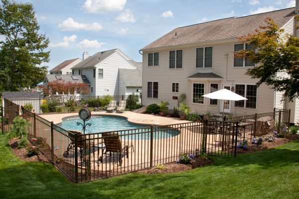 Lush, resort-like backyard swimming pool with a bronze pool fence surrounding it.