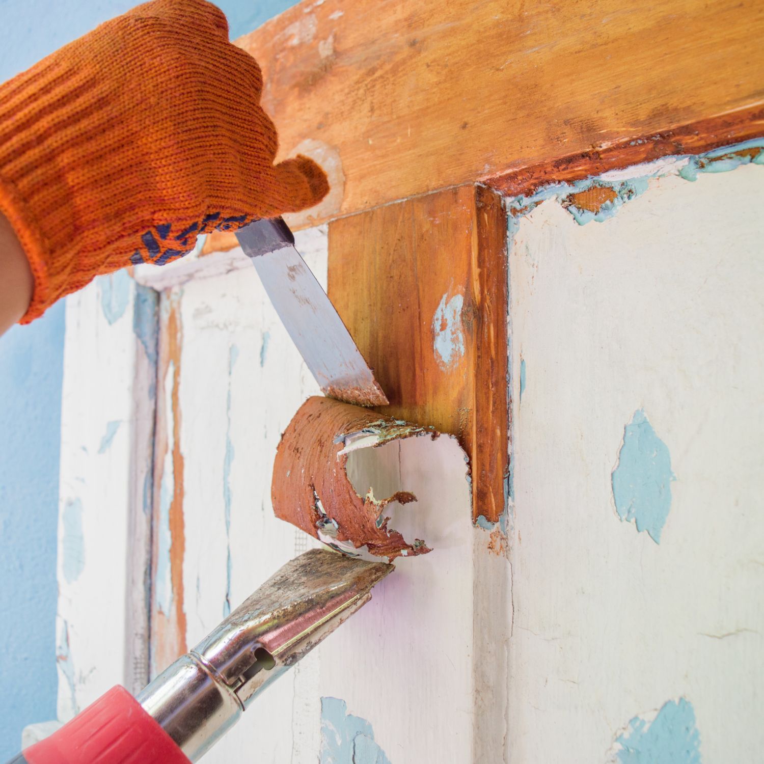 Removing paint from an old, wooden door frame with a scraper and a hair dryer.