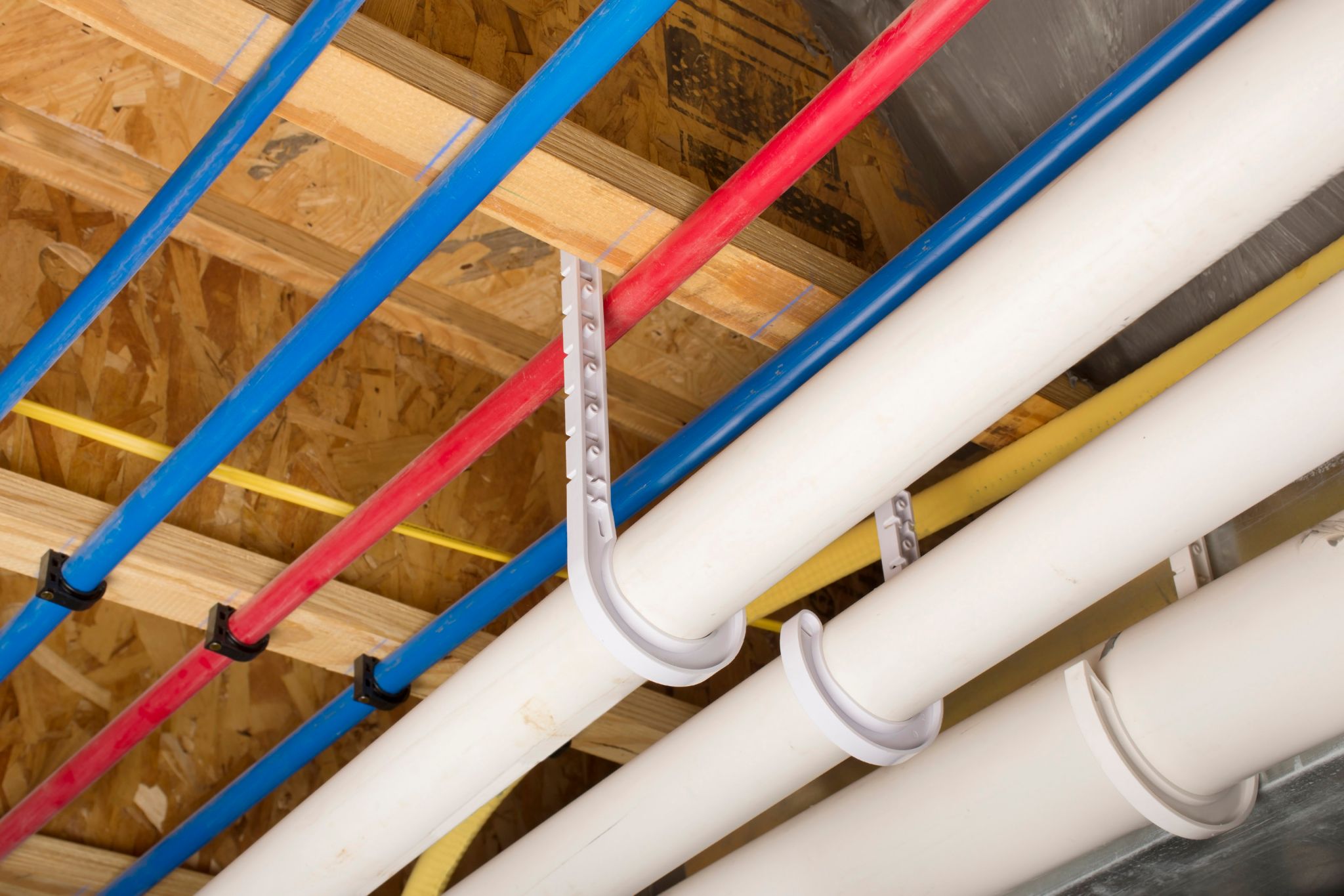 PEX plumbing pipes and drain pipes attached to the basement ceiling of a home.
