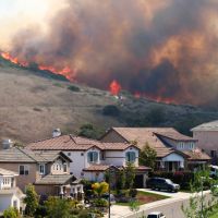 A large brush wildfire burning extremely close to several homes.