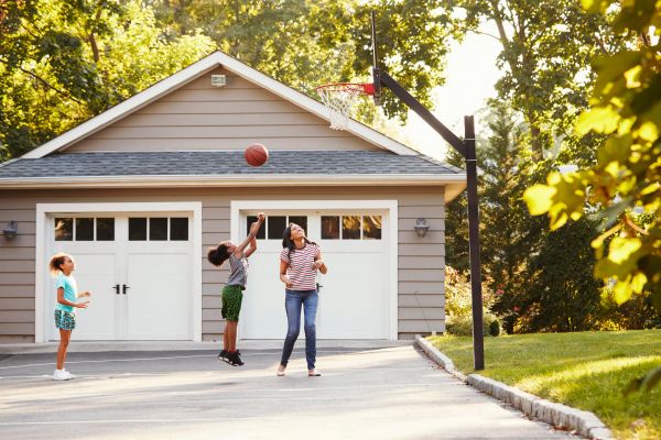 Mother And Children Playing Basketball On Driveway At Home.