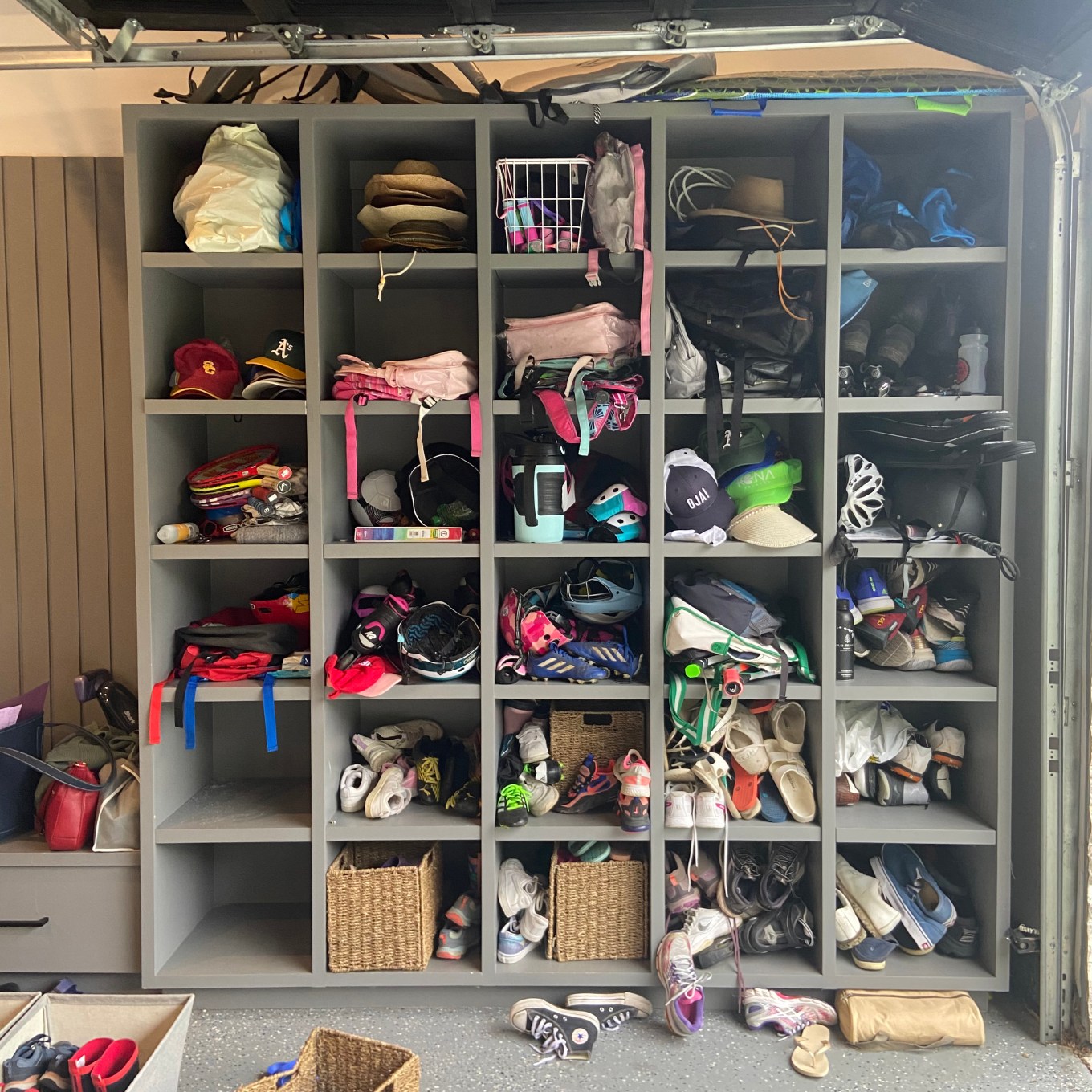 A before shot of messy shelves in a garage overflowing with sports equipment.