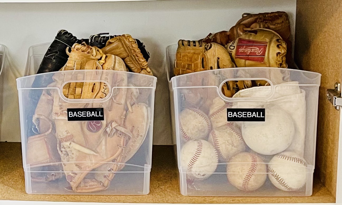 Clear storage bins with baseball equipment.