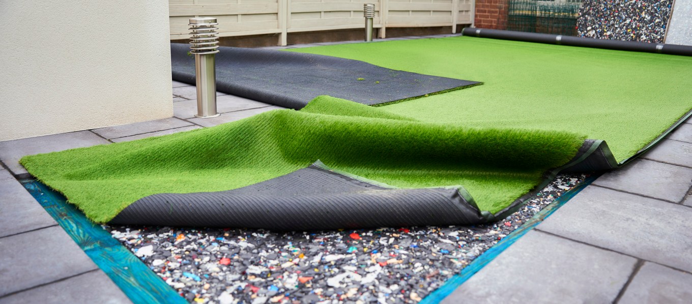 Artificial grass outside of a home with the underside showing shock pads or shock padding.