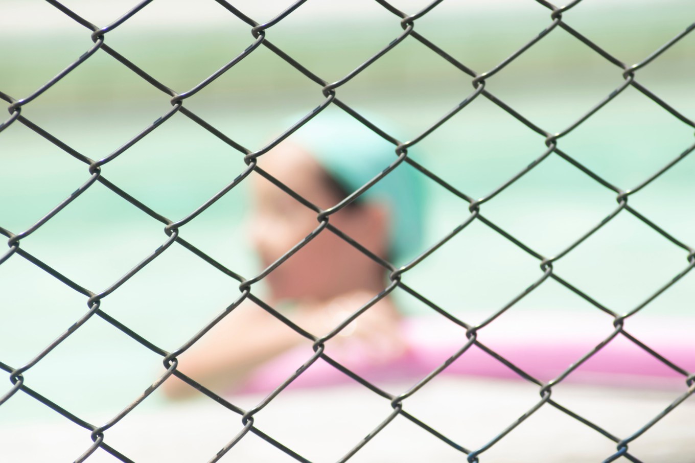 Close up of a chain link fence surrounding a swimming pool in a backyard.