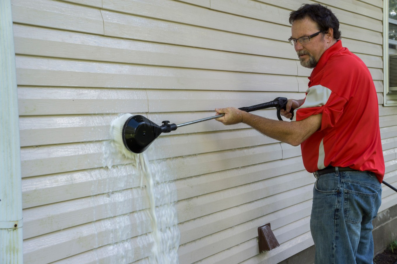 A man using a high pressure brush to remove algae and mold from vinyl siding.