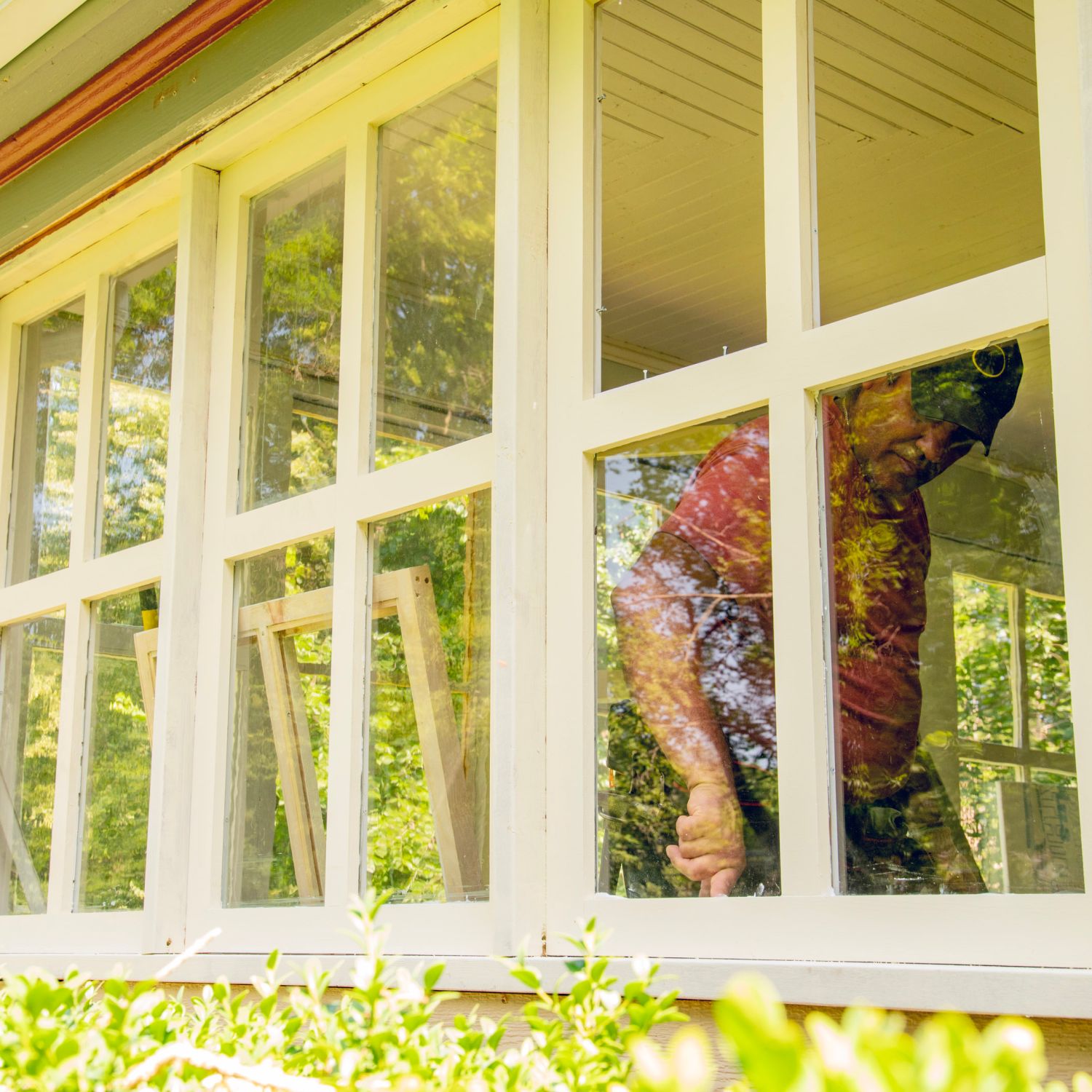 A homeowner replacing windows on a house and caulking to improve weatherproofing for winter.