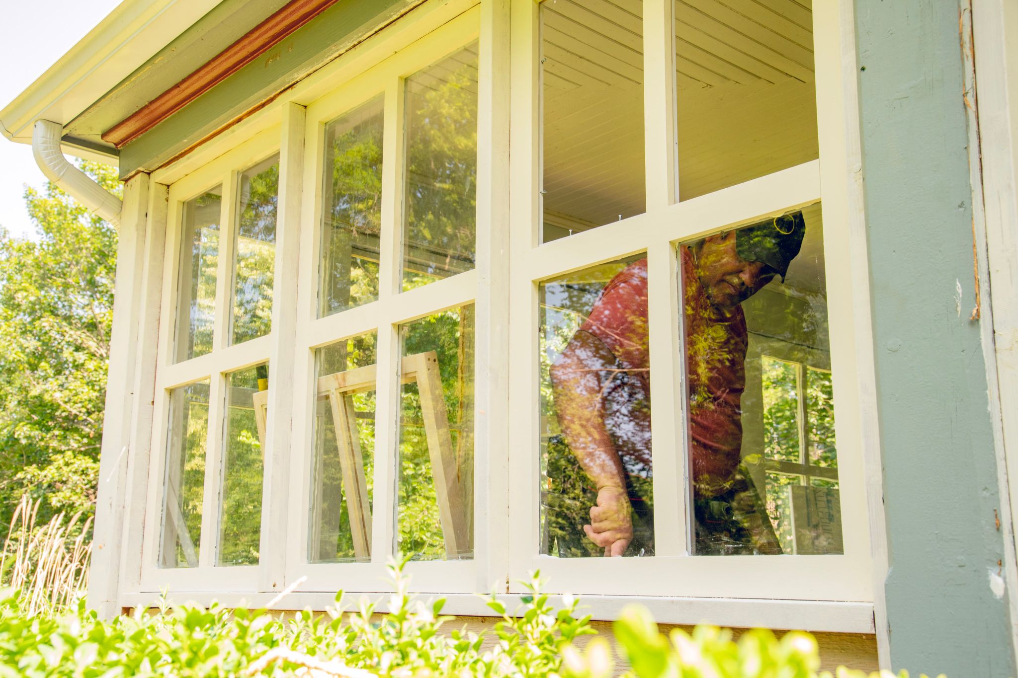 A homeowner replacing windows on a house and caulking to improve weatherproofing for winter.