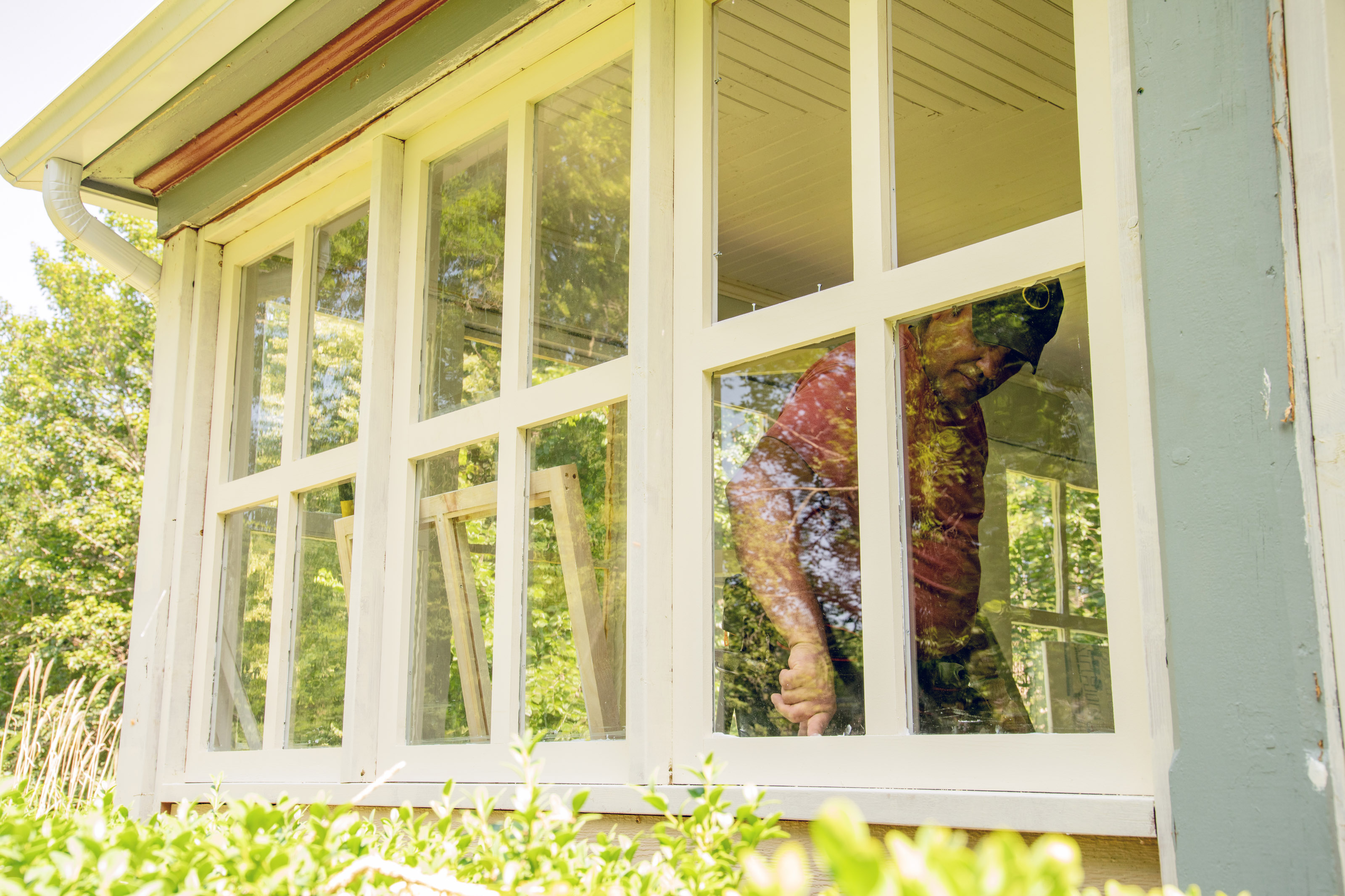 A homeowner replacing windows on a house and caulking to improve weatherproofing for winter.