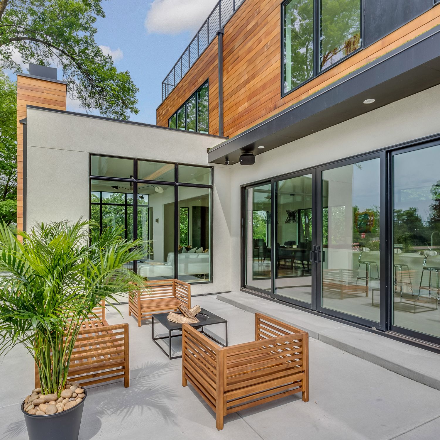 A modern, outdoor entertaining space featuring a patio, wooden chairs around a table, and a plant.