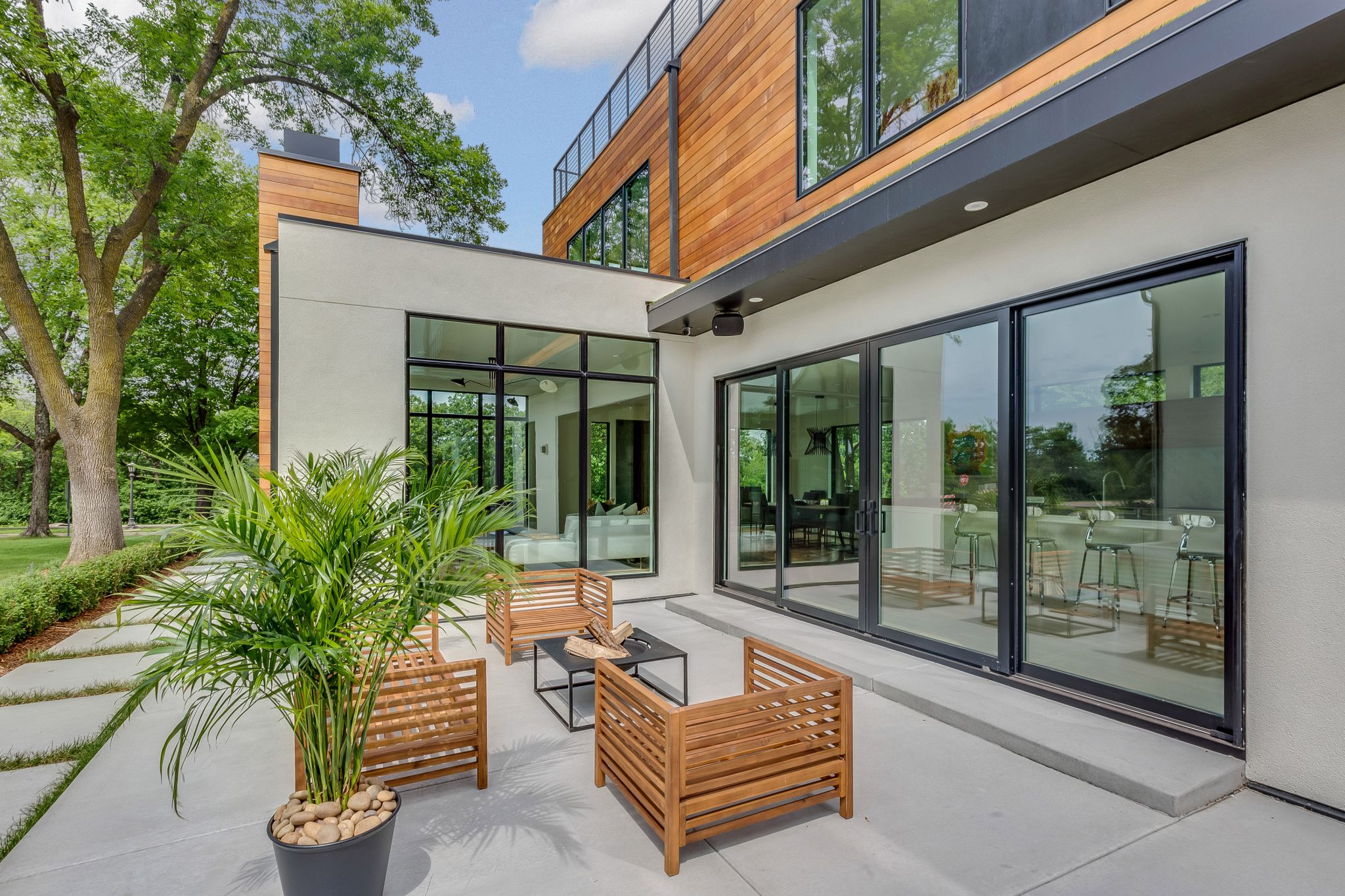 A modern, outdoor entertaining space featuring a patio, wooden chairs around a table, and a plant.