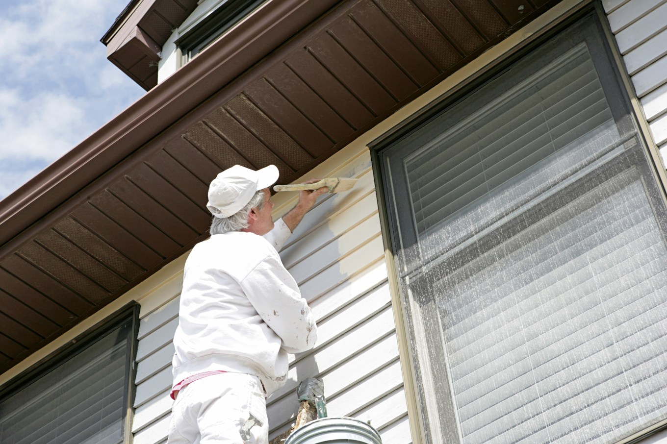 A person painting a second coat onto vinyl siding.