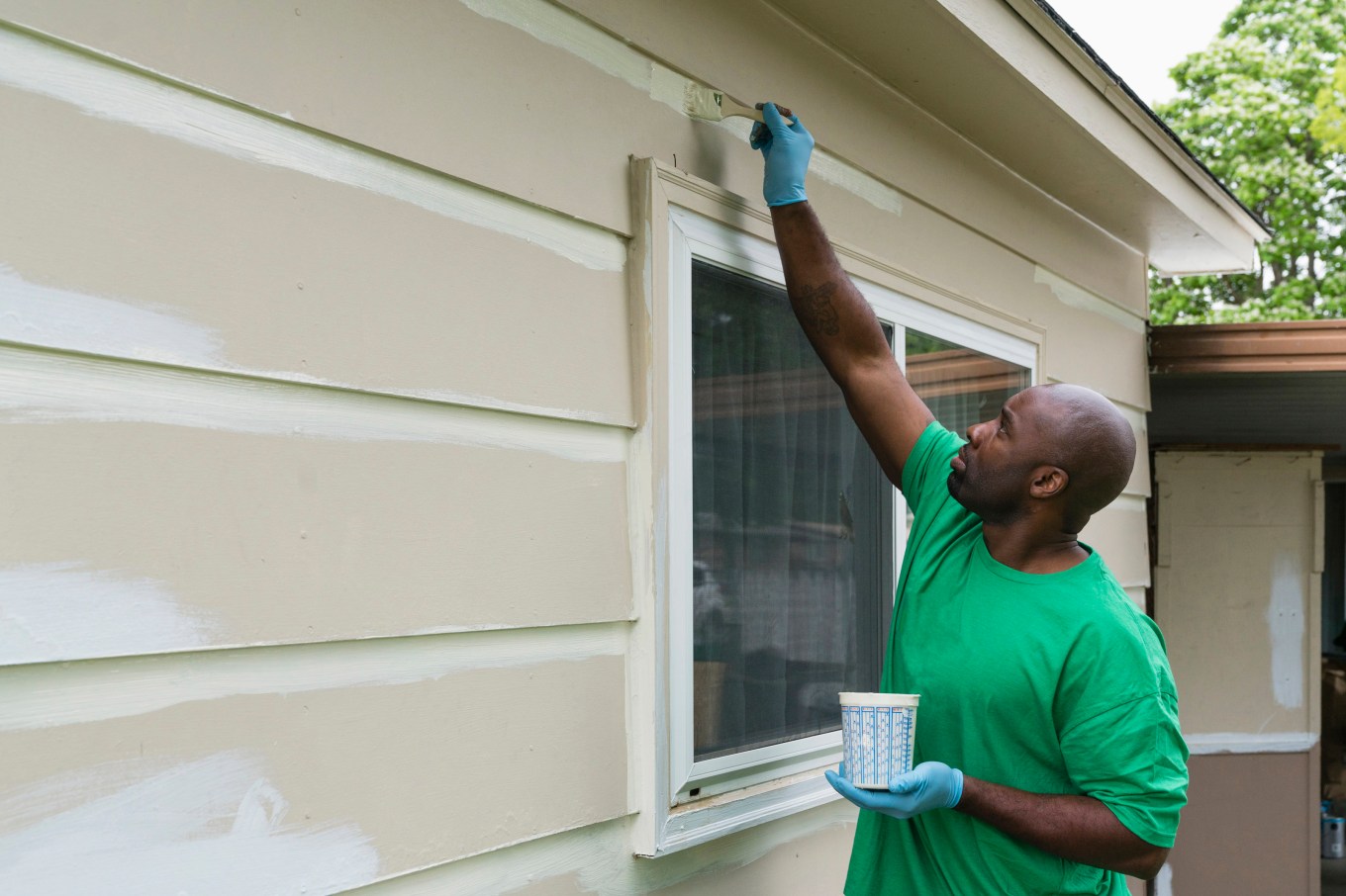 A person painting primer on top of vinyl siding.