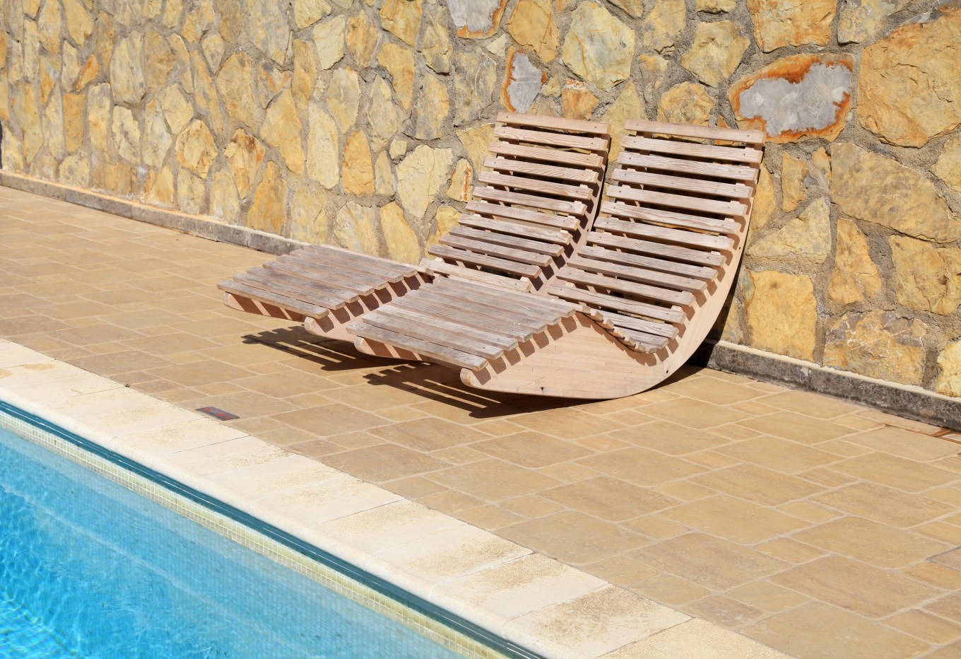 A stone fence surrounding a pool with lounge chairs.