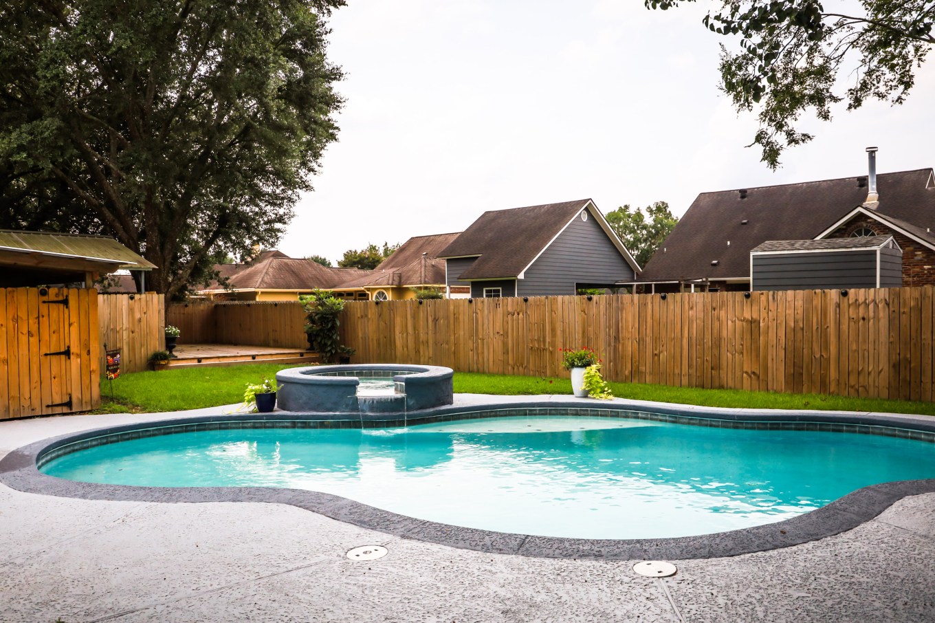 A wood fence surrounding a suburban backyard swimming pool.