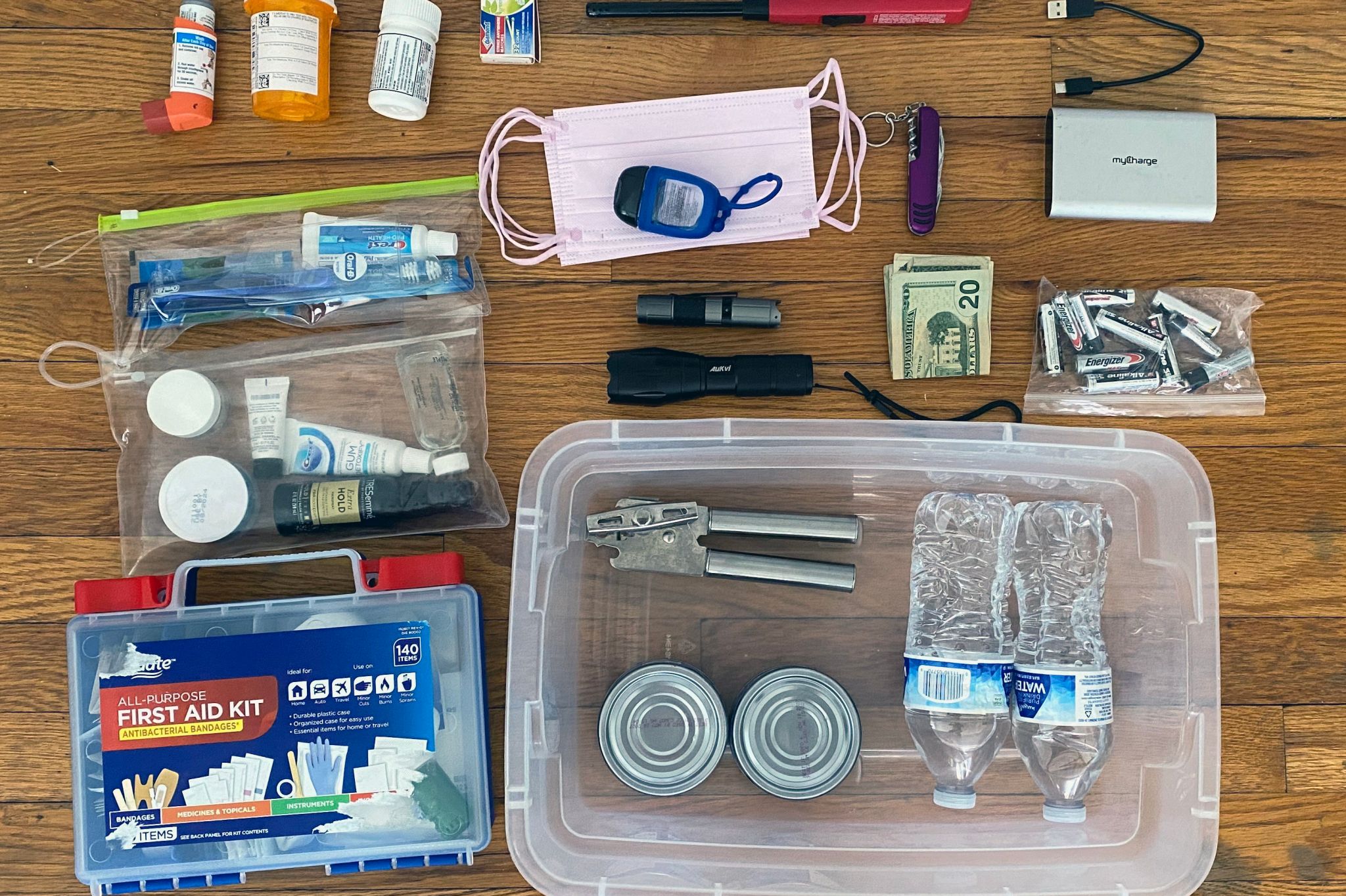 An emergency preparedness kit with a variety of important items in it like pills, a flashlight, first aid kit, batteries, money, and more.