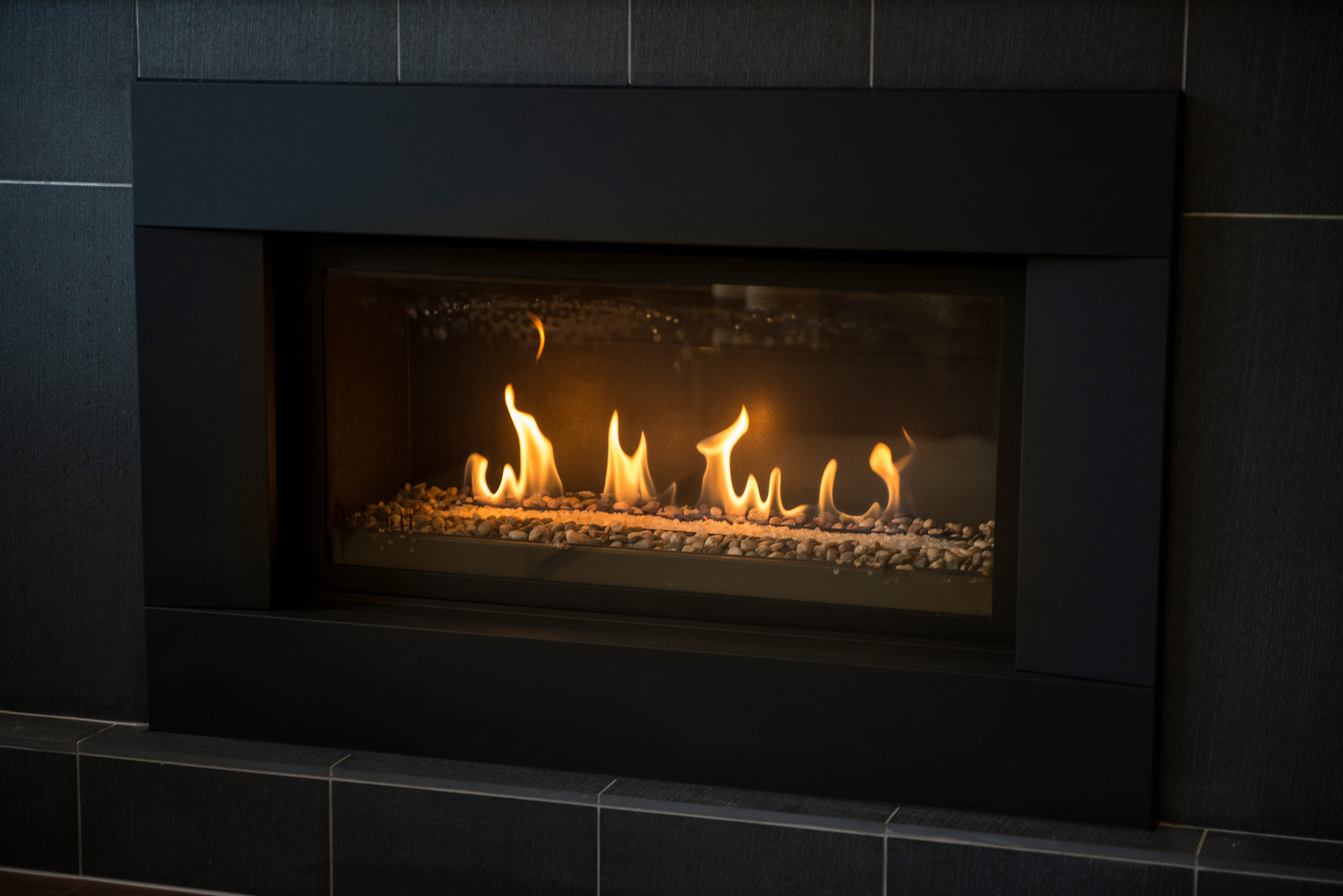 Modern gas fireplace with stones surrounded by black tile.