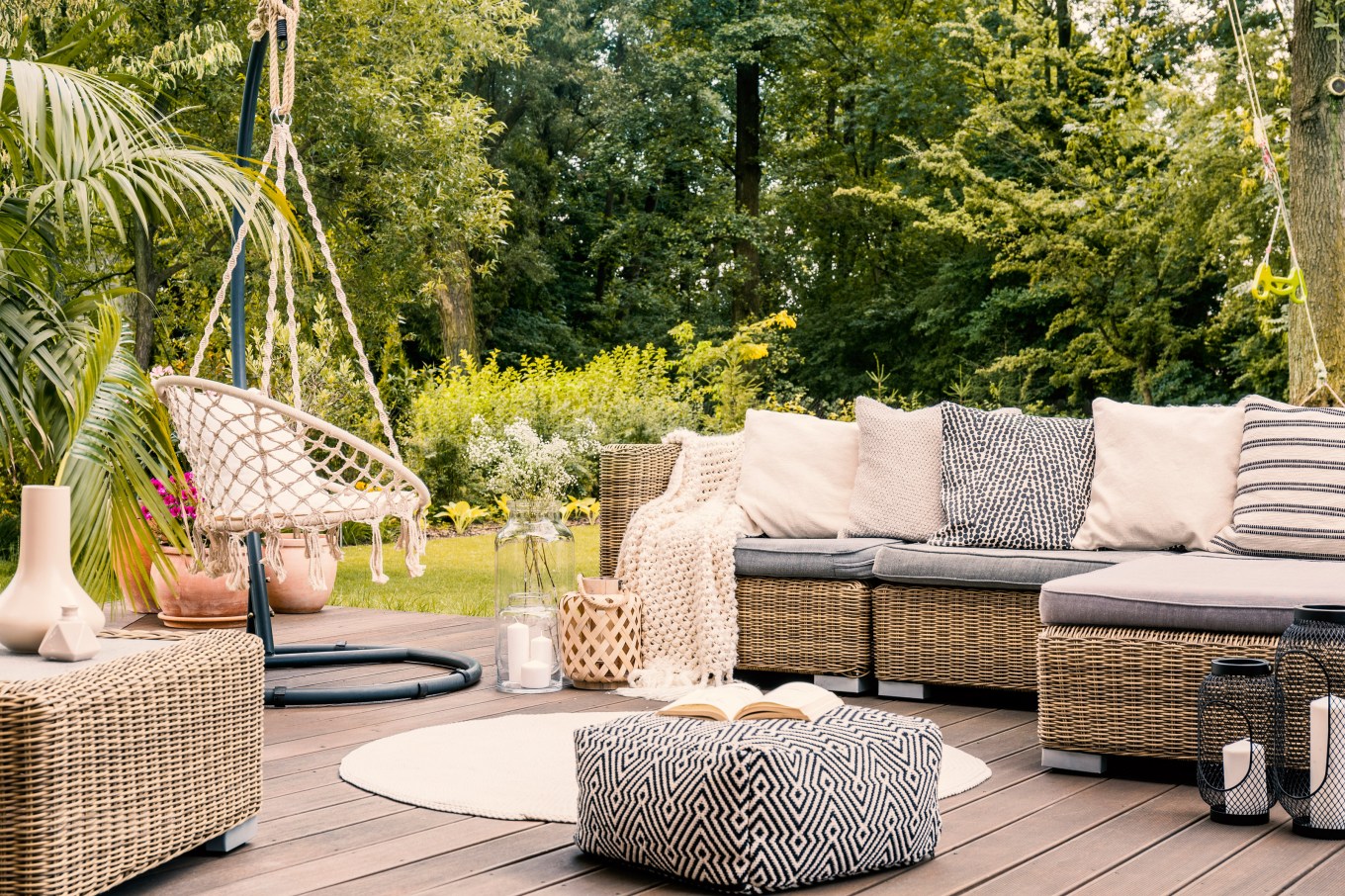 A bright terrace with a rattan corner sofa, hanging chair and round rug functions as an outdoor retreat.