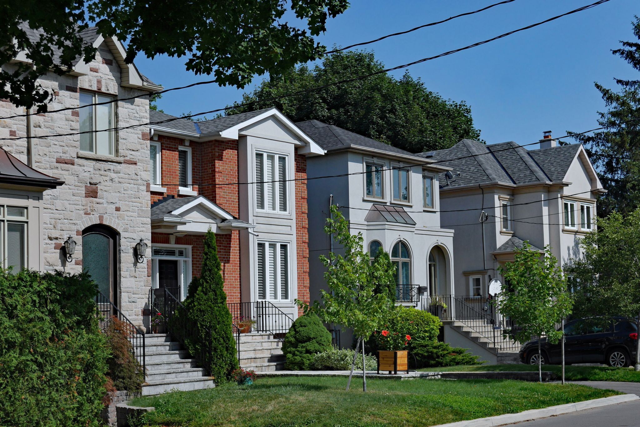 Street of large suburban detached houses with front yards on a sunny summer day.