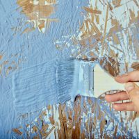 A paint brush being used to paint over paint that was partially scraped off, such as lead paint might be.