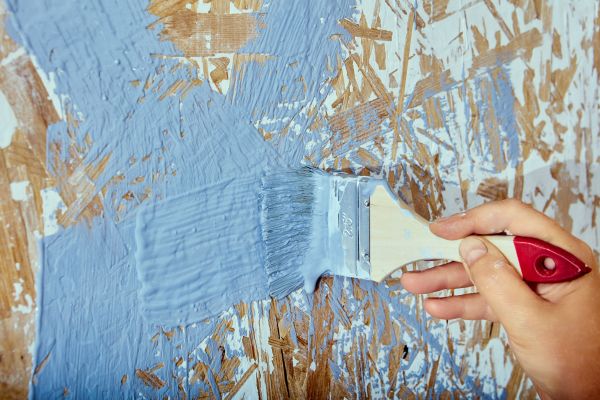 A paint brush being used to paint over paint that was partially scraped off, such as lead paint might be.