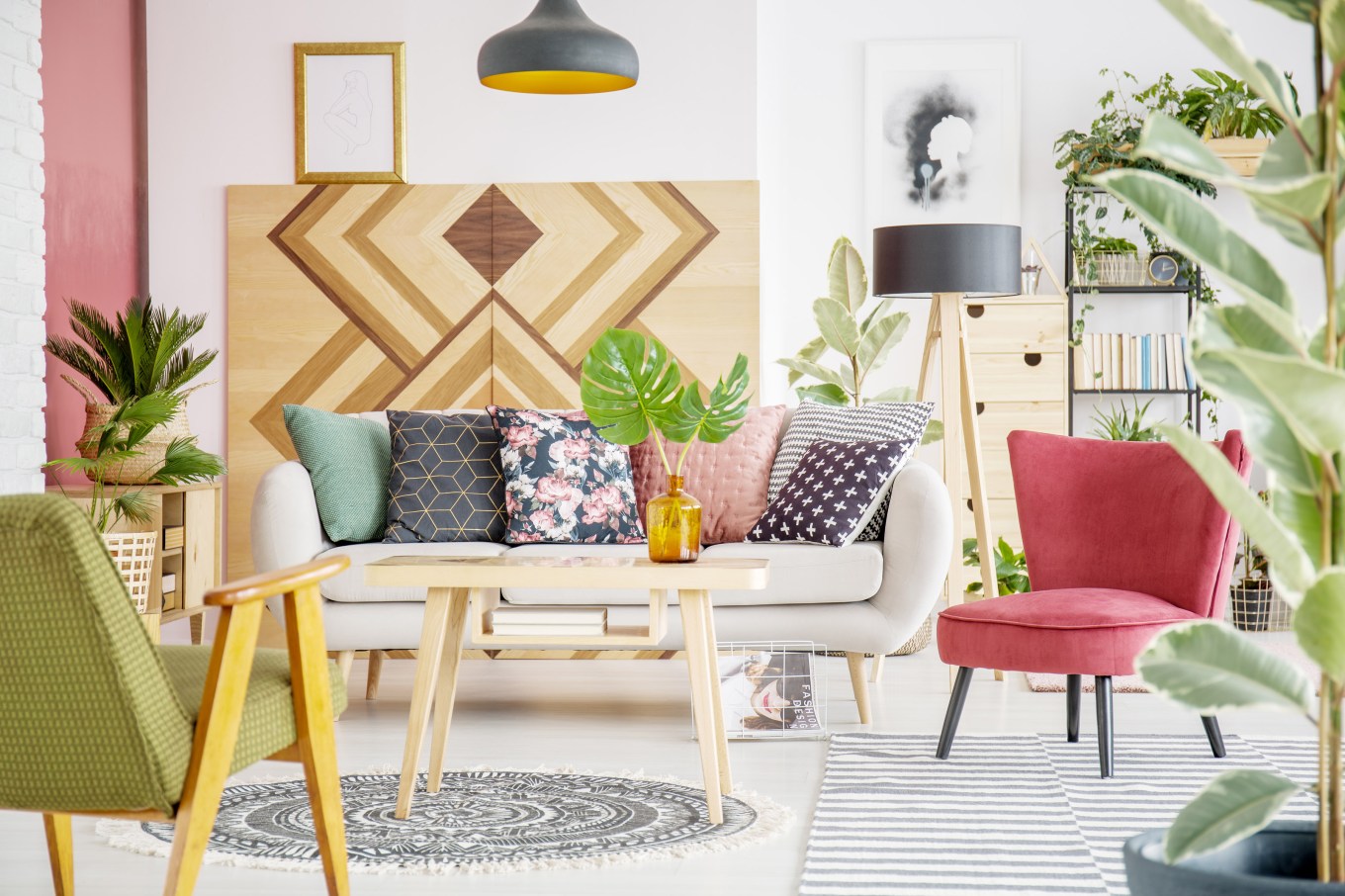 Patterned pillows on sofa next to red armchair in cozy living room interior with wooden furniture.