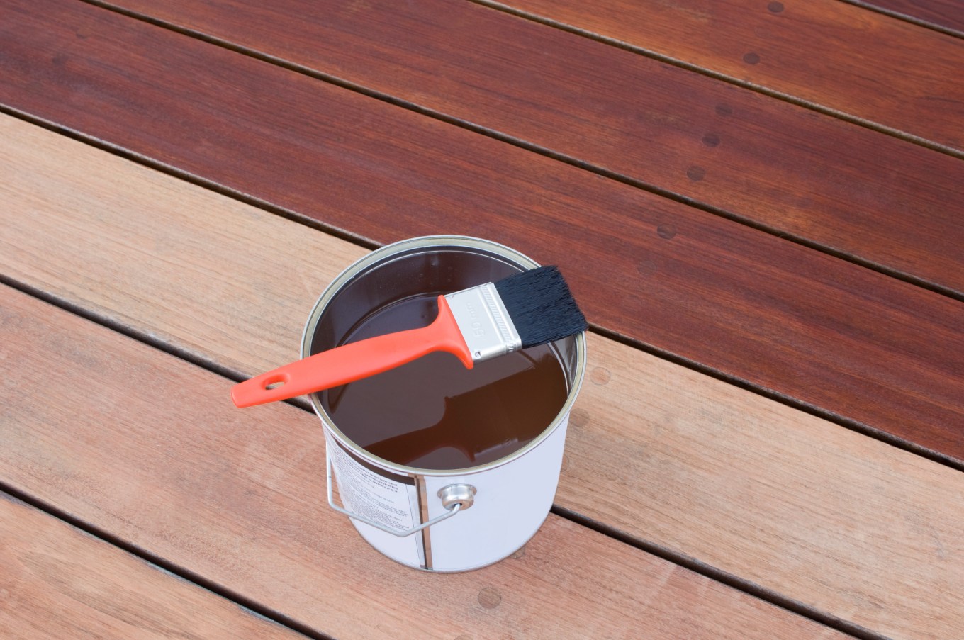 Exterior stain sitting in a can with a brush on an outside deck.